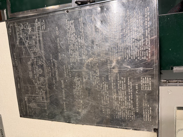 An engraved metal instruction plate mounted on a bulkhead lists operating procedures and diagrams for the bow and stern diving gear, covering venting, rigging, power and emergency tilting, and reference plans.