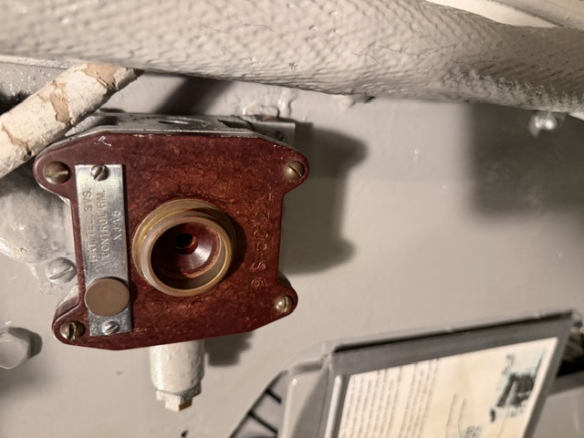 A bulkhead-mounted bakelite sound-powered telephone jack box bearing a metal plate reading 'BAT. TEL. SYS. CONTROL RM. XJ06,' with white lagged piping running alongside it at right.